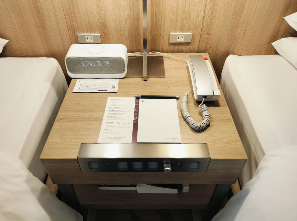 ベッドの間に電源やライトのスイッチ、時計、電話など。