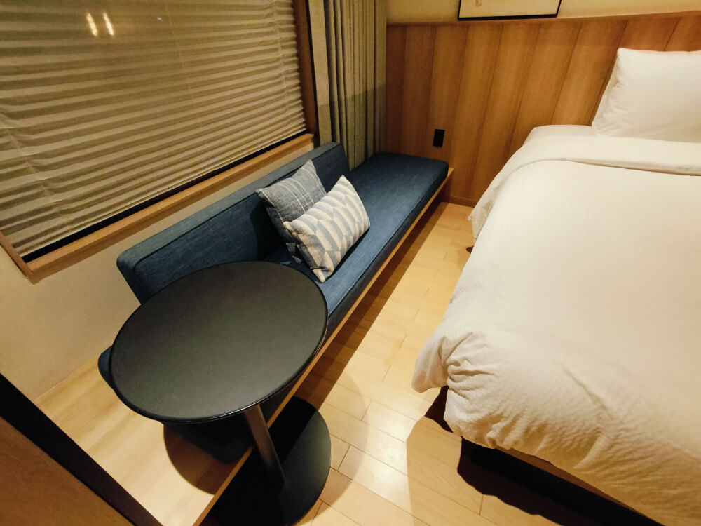 窓の前に小さな丸テーブルとソファ、クッションが二つ置いてある